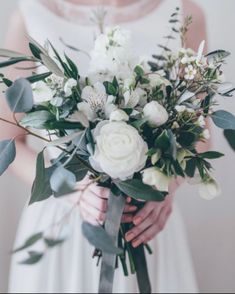 a woman holding a bouquet of white flowers and greenery