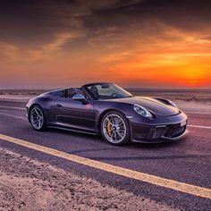 a purple sports car driving down the road at sunset or dawn with clouds in the background