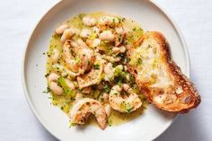 a white plate topped with pasta and shrimp next to a piece of toasted bread