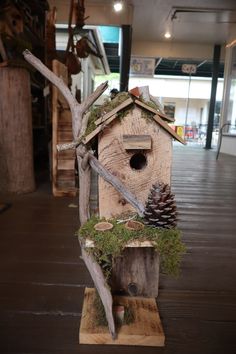 a birdhouse made out of wood with moss and pine cones on the roof is displayed