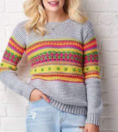 a woman wearing a colorful sweater standing in front of a brick wall with her hands on her hips