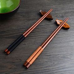 two chopsticks with wooden handles sit on a table next to a green bowl