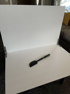 a pen sitting on top of a white table in front of a couch and window