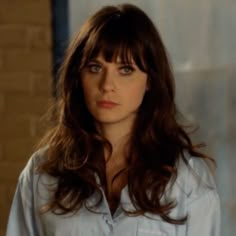 a woman with long brown hair and blue eyes looks at the camera while standing in front of a brick wall