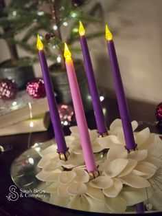 three candles are lit on a table with flowers and christmas tree in the back ground