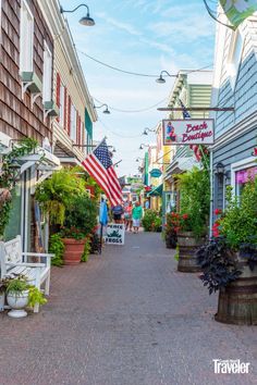 an american flag is hanging on the side of buildings in a small town with potted plants