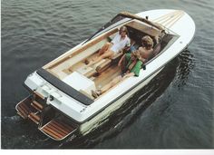 three people are sitting on the back of a boat in the water while another person sits at the front of the boat