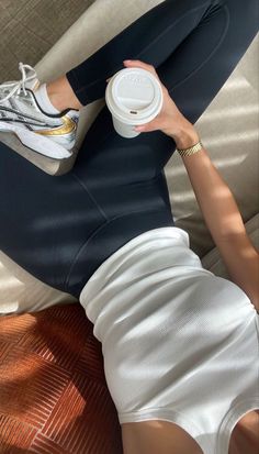 a woman laying on top of a bed holding a coffee cup in her right hand