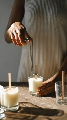 a woman is pouring some liquid into two glasses with cinnamon sticks sticking out of them