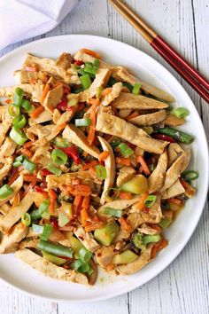 a white plate topped with chicken and veggies next to chopsticks