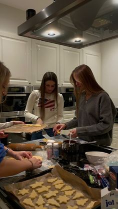 three women are making cookies in the kitchen