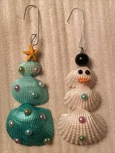 two seashell ornaments are hanging from hooks on a white cloth covered surface, one has a starfish and the other is a snowman