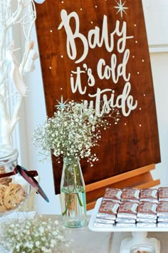 an image of baby it's cold outside sign and cookies on a table with flowers