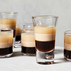 four shot glasses filled with liquid sitting on top of a white tablecloth next to each other