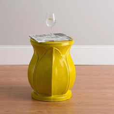 a yellow vase sitting on top of a wooden floor next to a glass filled with water