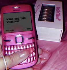 a pink cell phone sitting on top of a table next to a white box with the words what are you wearing?