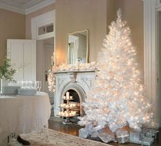 a white christmas tree with lit candles in front of a fireplace