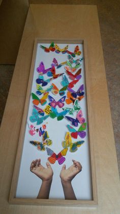 a wooden frame filled with lots of different colored paper butterflies on top of a floor