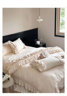 a bed with white ruffles and pillows on it in front of a window