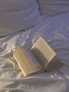 an open book laying on top of a white bed sheet covered in sheets and pillows