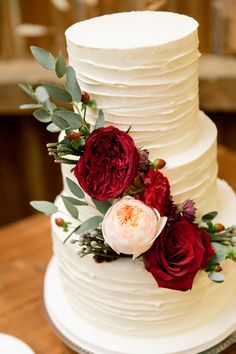 a three tiered white cake with red flowers and greenery