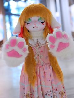 a doll with orange hair and green eyes is dressed in a pink dress, holding her hands up