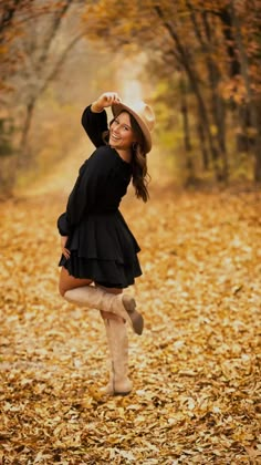 a woman wearing boots and a hat is dancing in the fall leaves with her hands behind her head