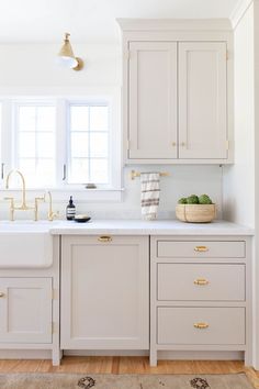 a kitchen with white cabinets and gold hardware on the handles, sink, and window