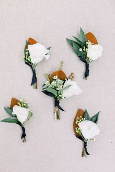 four boutonnieres with white flowers and green leaves