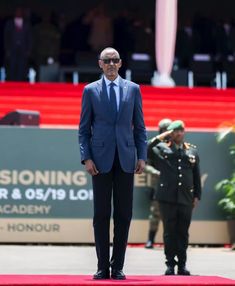 a man in a suit and tie standing on a red carpet with other people behind him