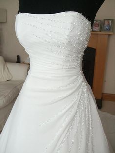 a white wedding dress is displayed on a mannequin in front of a couch