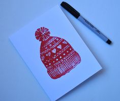 a red and white card with a knitted hat on it next to a marker