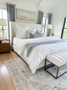 a large white bed sitting in a bedroom on top of a hard wood floor next to a window