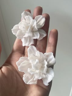 two white flowers are in the palm of someone's hand and they appear to be real