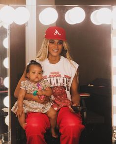 a woman sitting in front of a mirror holding a small child and wearing red pants