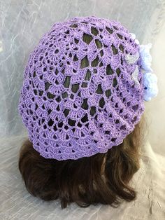 a woman wearing a purple crocheted hat with flowers on it's brim