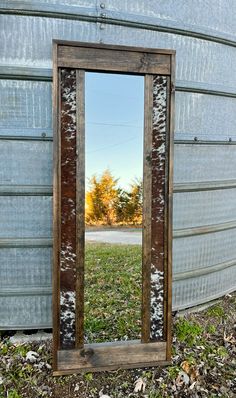 an old mirror sitting on the ground in front of a metal structure with grass and trees