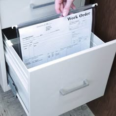 a person holding a file cabinet with work order paper in it's bottom drawer