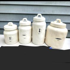 four white canisters sitting on top of a table next to each other in front of a house