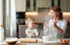 a woman and child in the kitchen with flour being sprinkled on their hands