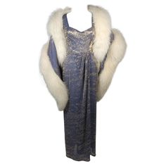 This Nolan Miller attributed gown with wrap ensemble is composed of a slate blue silk and gold lame. The gown is in excellent condition and features a center back zipper. The large wrap is in need of reconstruction, the fur is in poor condition and should be replaced. The silk portion of the wrap is in excellent condition. We have a furrier whom can redo the fox for approximately $2000.00 USD. This is a stunning ensemble. This ensemble is a custom couture designed piece and is not labelled. The 1920s Evening Gowns, Nolan Miller, Runway Gowns, Luxurious Dresses, Le Specs, Couture Vintage, Vintage Style Dresses, Glamour Fashion, White Fox