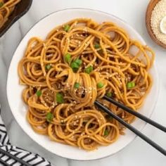 noodles with mushrooms and peas in a white bowl on top of a marble table next to black chopsticks