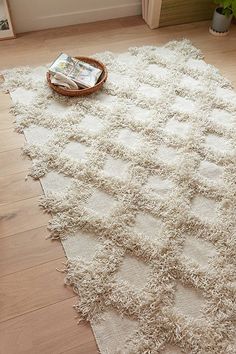 a white rug on the floor with a basket next to it and magazines in front of it