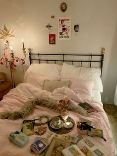 a bed covered in lots of books on top of a pink blanket next to a lamp