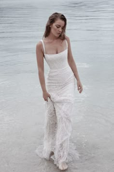 a woman standing on top of a beach next to the ocean wearing a white dress