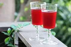 two glasses filled with red liquid sitting on top of a wooden table