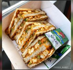 a box filled with sandwiches sitting on top of a table next to a bag of chips