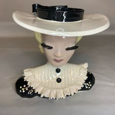 a ceramic head wearing a white hat with black trim and pearls on the brim