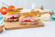 a ham and cheese sandwich cut in half on a cutting board next to some tomatoes