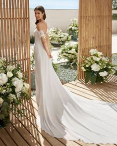 a woman in a white dress standing on a wooden platform with flowers and greenery